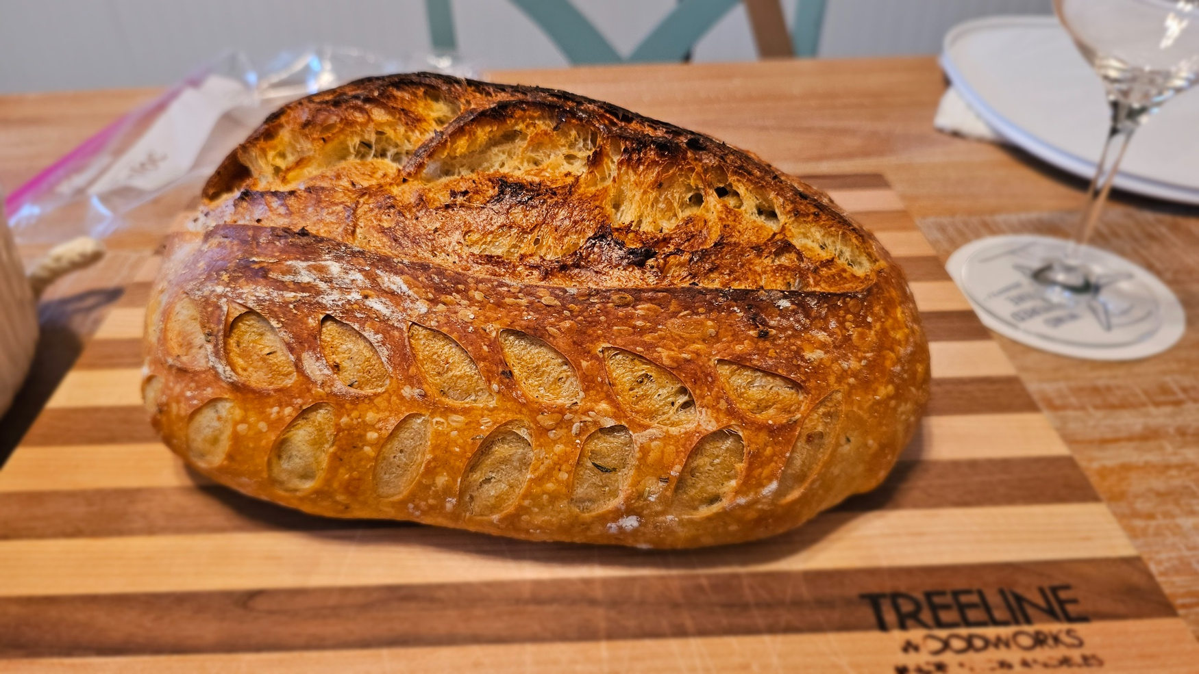 Homemade artisan sourdough loaf with detailed leaf scoring on a striped wooden board