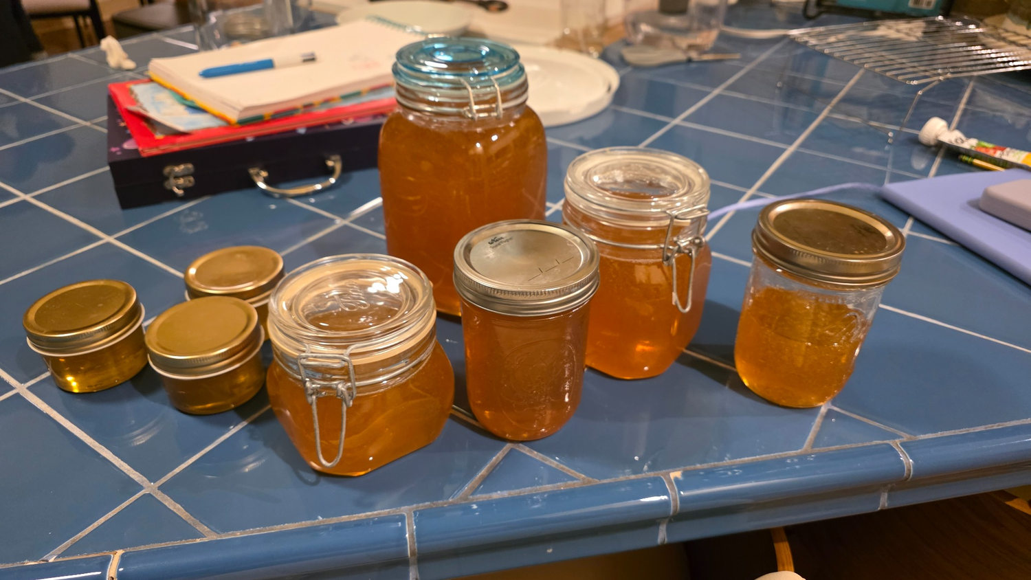 A selection of golden honey in glass jars on a blue tiled countertop
